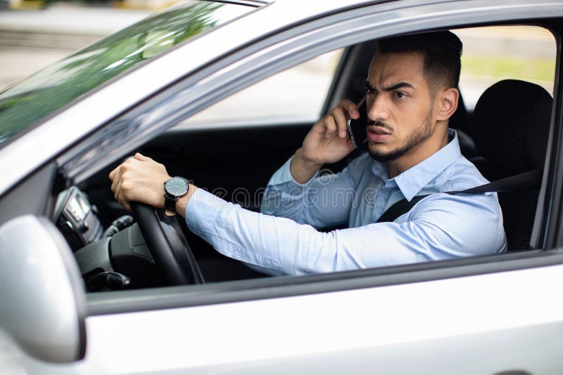 Un hombre árabe enojado que lucha por teléfono mientras conduce un auto fotografía de archivo