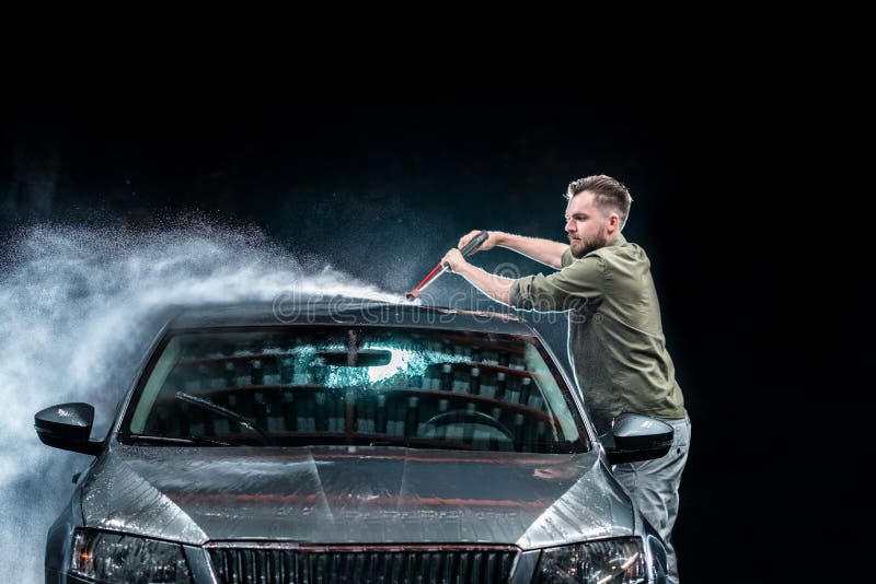 Un homme avec un joint de barbe ou de voiture lave une voiture grise avec un joint à haute pression la nuit dedans de rue photo stock Un homme avec un joint de barbe ou de voiture lave une voiture grise avec un joint à haute pression la nuit dedans de rue photo stock