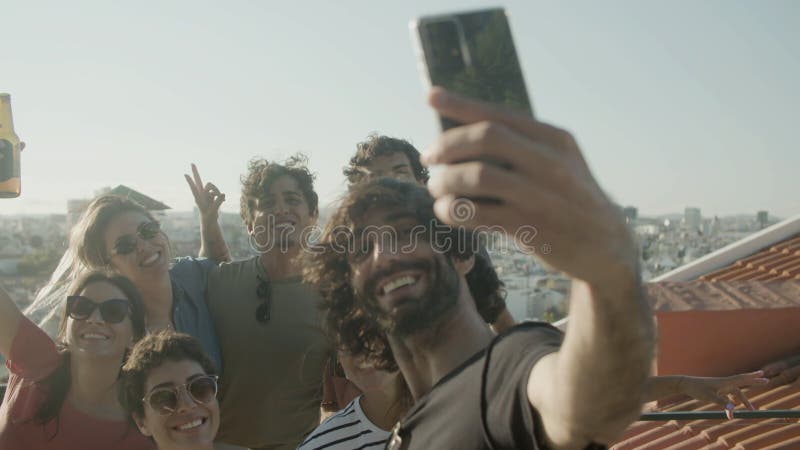 Un homme barbu heureux prenant une photo avec des amis sur le toit banque de vidéos