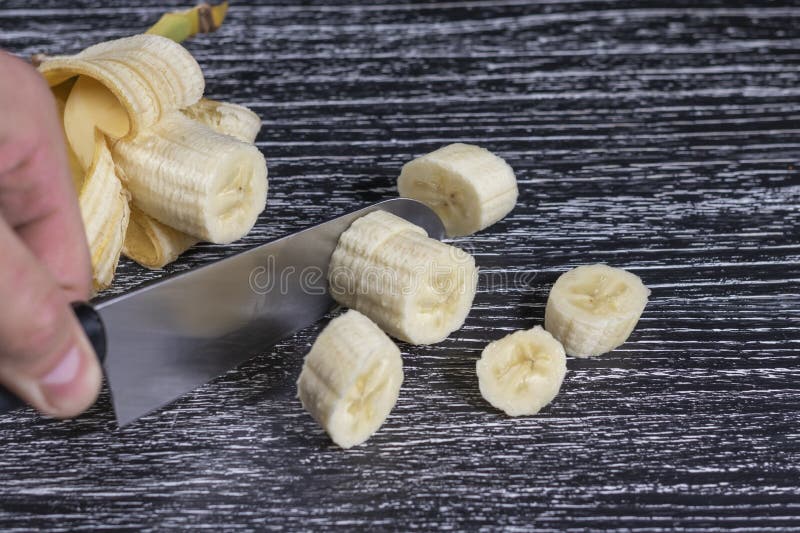 Un homme coupe un couteau de banane en tranches sur une vieille table en bois noire photographie stock libre de droits Un homme coupe un couteau de banane en tranches sur une vieille table en bois noire photographie stock libre de droits
