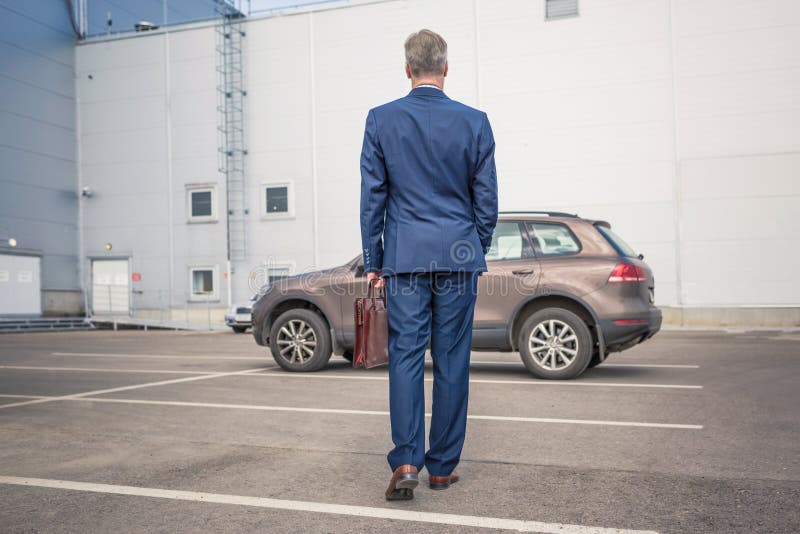 Un homme d'affaires d'âge moyen en costume bleu riant en appelant par téléphone de sa voiture sur le parking privé de la grande u images stock Un homme d'affaires d'âge moyen en costume bleu riant en appelant par téléphone de sa voiture sur le parking privé de la grande u images stock