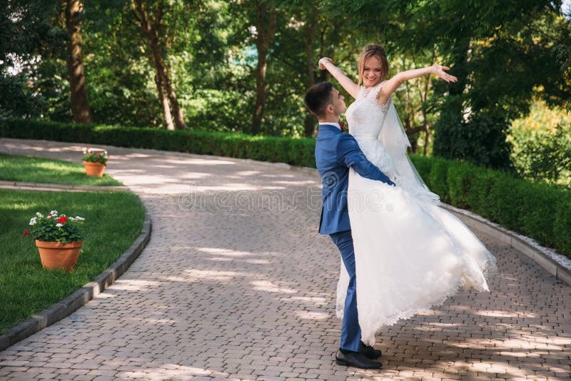 A men in a classic suit turns his bride. the guy lifted the girl in his arms and loves looking at her, she raised her hands to the sky and smiles, they are happy. A men in a classic suit turns his bride. the guy lifted the girl in his arms and loves looking at her, she raised her hands to the sky and smiles, they are happy