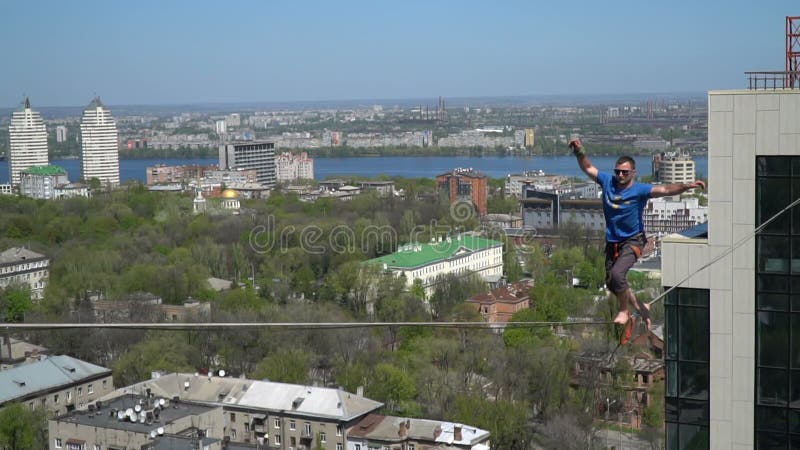 Un homme dans un T-shirt bleu se tient doucement sur une corde serrée à la haute altitude banque de vidéos