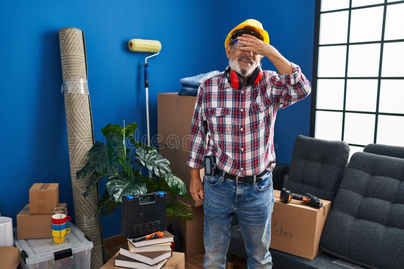 Un homme de haut niveau joyeux qui cache les yeux derrière la main pour une surprise tout mis en casque dur et lunettes de sécurit photo libre de droits