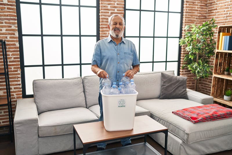 Un homme de haut niveau joyeux qui tourne un clin d'oeil flirté vers la caméra tout en recyclant joyeusement les bouteilles en pla photographie stock