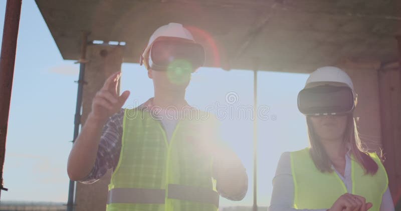 Un homme et ingénieurs d'une femme à un chantier de construction en verres de VR contrôler la construction d'un bâtiment discutan