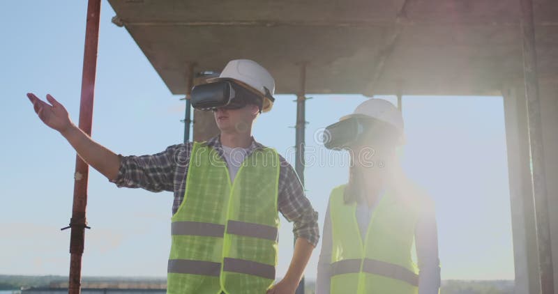 Un homme et ingénieurs d'une femme à un chantier de construction en verres de VR contrôler la construction d'un bâtiment discutan