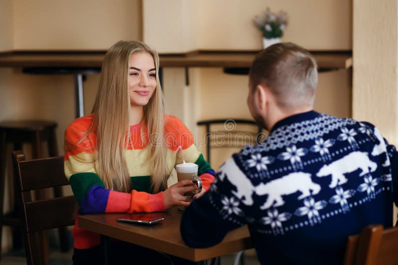 Un homme et une femme s'asseyent dans un café et le café potable, un couple utilisent les chandails de fantaisie, une fille souri photographie stock Un homme et une femme s'asseyent dans un café et le café potable, un couple utilisent les chandails de fantaisie, une fille souri photographie stock