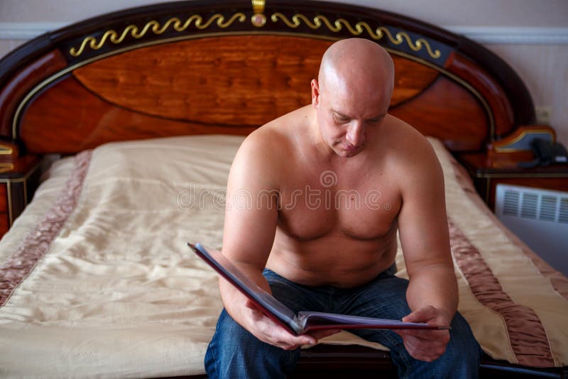 Un homme s'asseyant sur le lit et lisant un magazine photos libres de droits Un homme s'asseyant sur le lit et lisant un magazine photos libres de droits