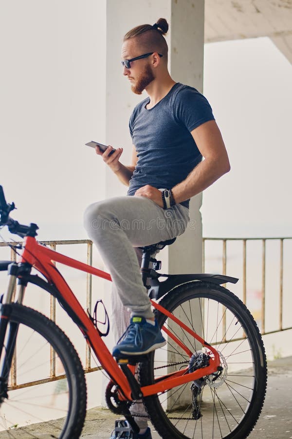 Un homme s'assied sur une bicyclette rouge de montagne et tient un smartphone photographie stock libre de droits