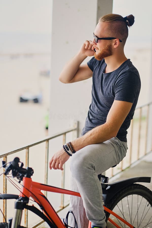 Un homme s'assied sur une bicyclette rouge de montagne et tient un smartphone images libres de droits
