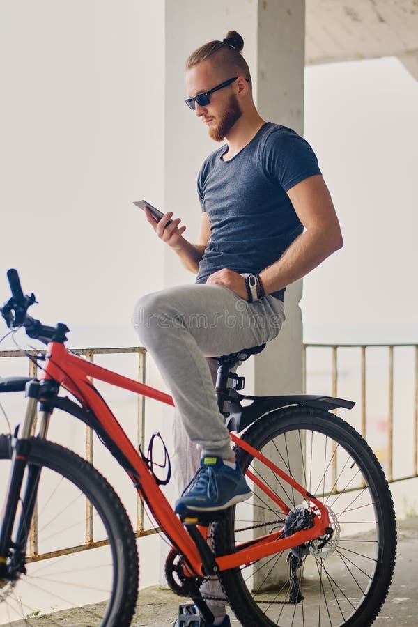 Un homme s'assied sur une bicyclette rouge de montagne et tient un smartphone photo stock