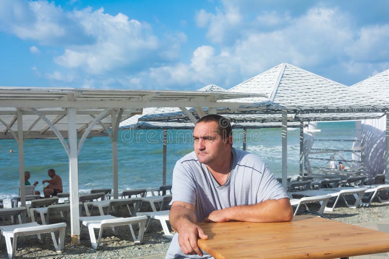 Un homme s'assoit à une table vide par beau temps sur la plage. vacances d'été photos stock
