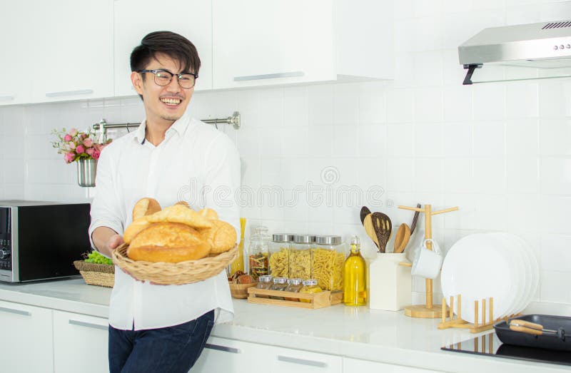 A cute man is holding breads and standing in the kitchen with happy. A cute man is holding breads and standing in the kitchen with happy