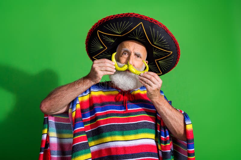 Un homme âgé gai en costume mexicain tenant une moustache de banane sur un fond vert vibrant photo stock