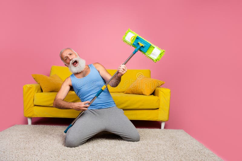 Un homme âgé qui prétend avec enthousiasme jouer de la guitare sur la flûte dans un intérieur coloré photographie stock libre de droits