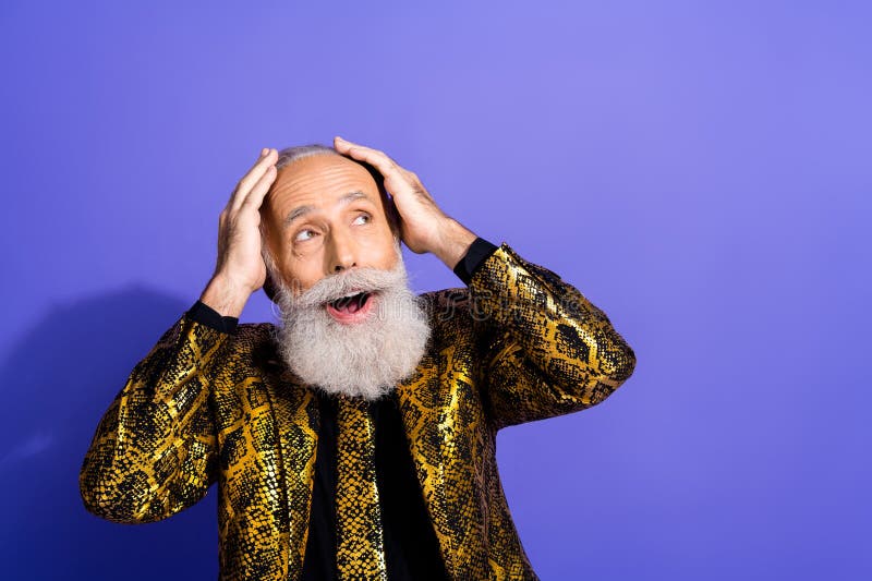 Un homme âgé élégant avec une barbe blanche portant une veste à motifs or sur fond violet photographie stock