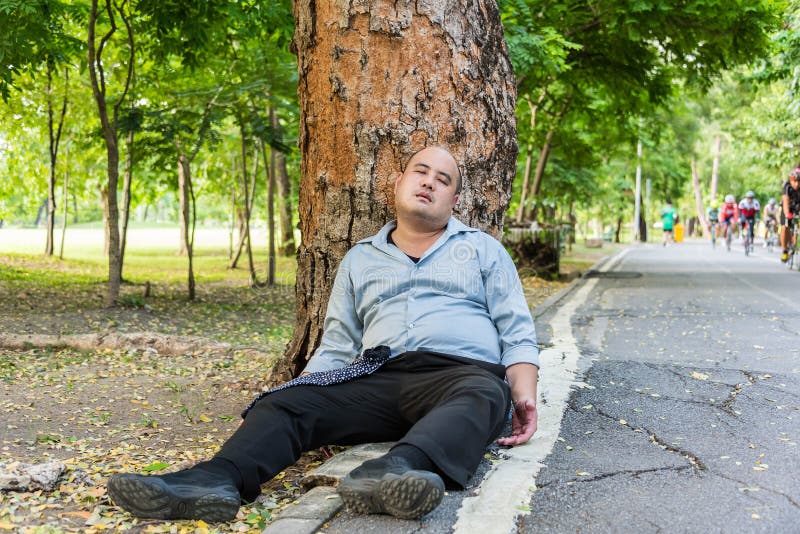 Un individuo asiático gordo que duerme debajo del árbol al lado de la calle foto de archivo Un individuo asiático gordo que duerme debajo del árbol al lado de la calle foto de archivo