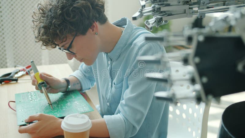 Un ingénieur robotique qui fabrique un microcircuit robotisé avec du fer à souder en salle de travail