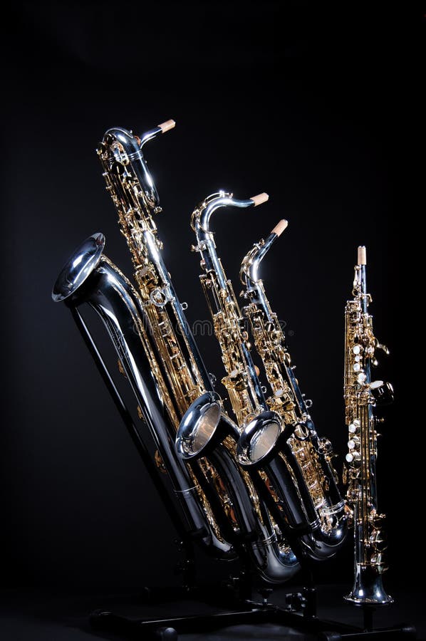 A set of four saxophones including a baritone, tenor, alto, and soprano isolated against a black background in the vertical format with copy space. A set of four saxophones including a baritone, tenor, alto, and soprano isolated against a black background in the vertical format with copy space.