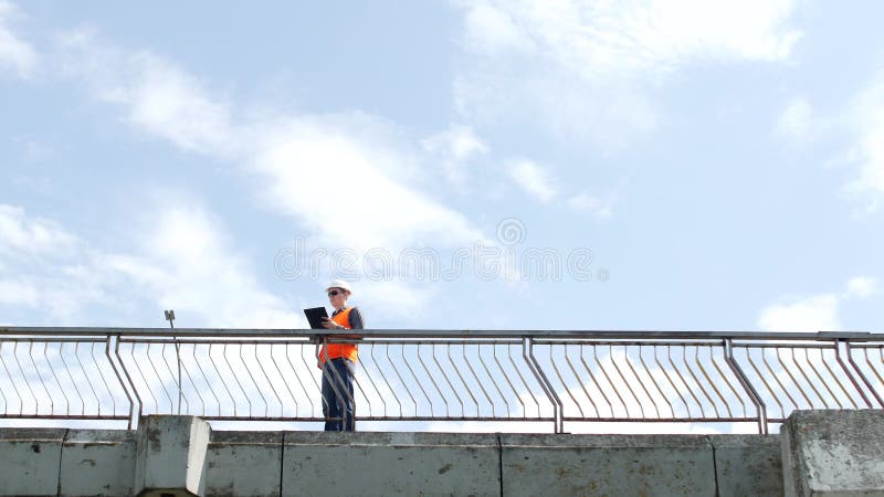 Un inspector del hombre camina a través del puente que mira alrededor y examina la calidad del puente, controles, ingeniero