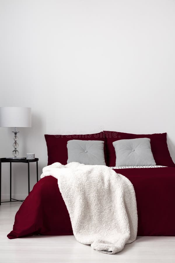 Un intérieur minimalistic de chambre à coucher avec un lit s'est habillé dans la toile de Bourgogne, les coussins piqués par gris images stock Un intérieur minimalistic de chambre à coucher avec un lit s'est habillé dans la toile de Bourgogne, les coussins piqués par gris images stock
