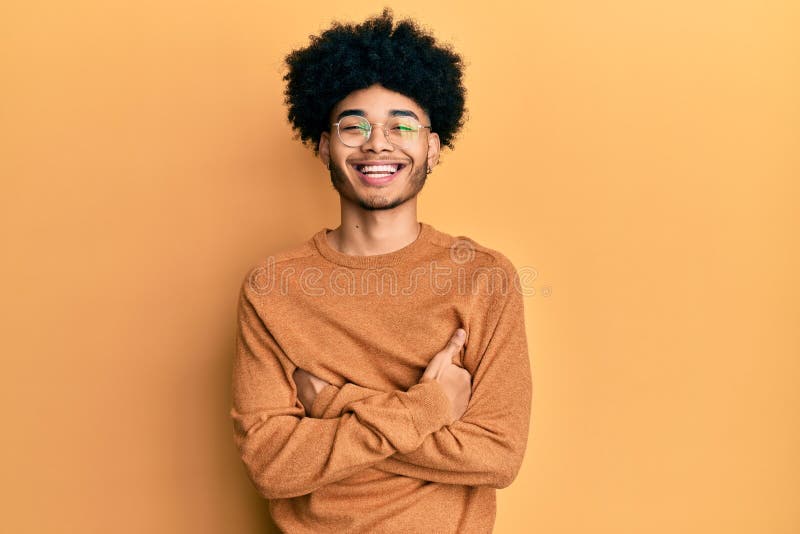 Un jeune afro-américain aux cheveux afro portant un pull d'hiver décontracté visage joyeux souriant aux bras croisés regardant la photographie stock