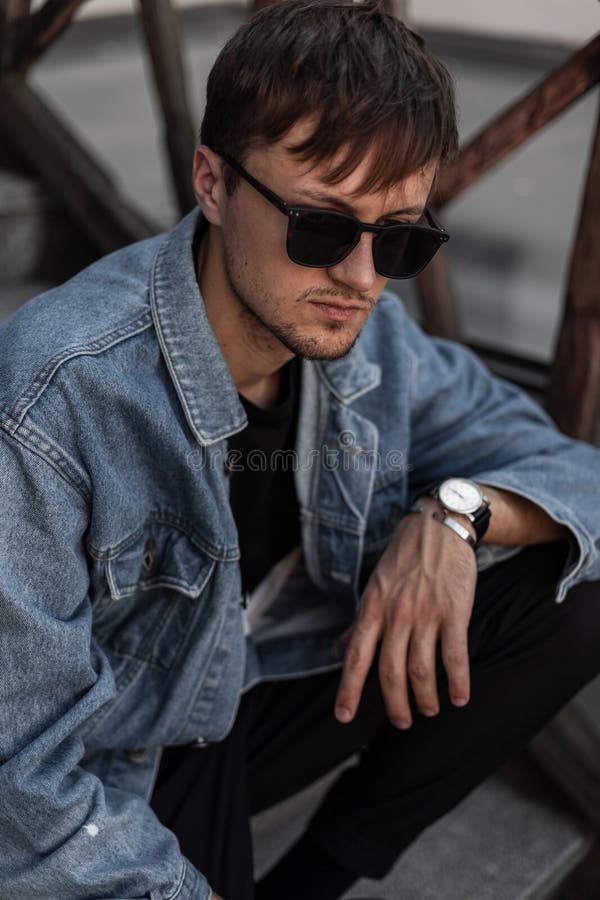 Un jeune branché branché branché branché vêtu de denim et de lunettes de soleil noires s'installe dans un escalier vintage de la photographie stock Un jeune branché branché branché branché vêtu de denim et de lunettes de soleil noires s'installe dans un escalier vintage de la photographie stock