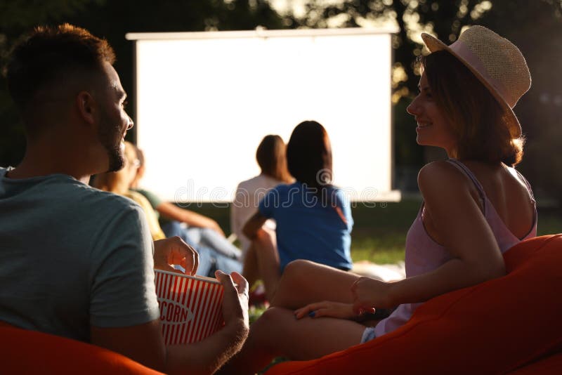 Young couple with popcorn watching movie in open air cinema. Space for text. Young couple with popcorn watching movie in open air cinema. Space for text