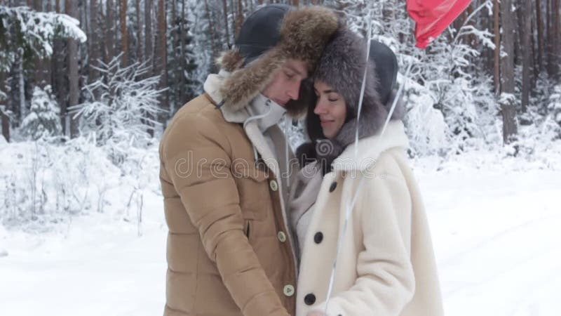 Un jeune couple heureux titulaire l'une en face de l'autre et s'embrasser dans une forêt neigeuse d'hiver. La fille détient les ba banque de vidéos