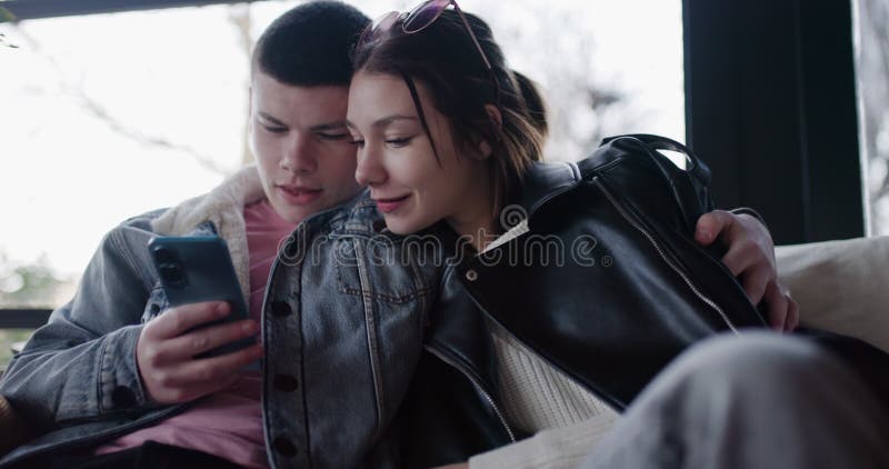 Un jeune couple se mange sur un canapé Partage rit en parcourant les médias sociaux sur Smartphone clips vidéos