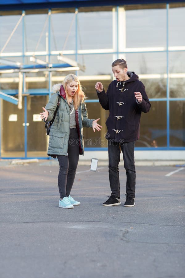 Un jeune couple, se tenant sur la rue et observant le smartphone en baisse sur l'asphalte images libres de droits Un jeune couple, se tenant sur la rue et observant le smartphone en baisse sur l'asphalte images libres de droits