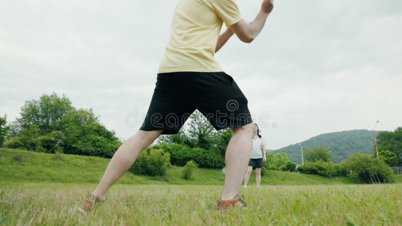 Un jeune couple une femme et un homme jouant à badminton. mouvement lent. vue en angle faible à travers les jambes mâles. été clips vidéos