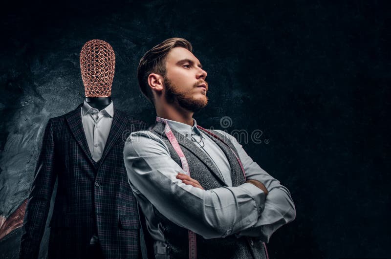 Un jeune couturier sûr posant à côté d'un mannequin dans le costume des hommes faits sur commande exclusifs dans un tailleur fonc photographie stock Un jeune couturier sûr posant à côté d'un mannequin dans le costume des hommes faits sur commande exclusifs dans un tailleur fonc photographie stock