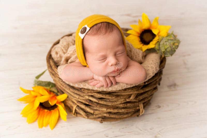Un jeune garçon mignon dort dans un chapeau jaune dès les premiers jours de la vie. Un mignon nouveau-né dort en chapeau jaune dans les premiers jours de la vie. sur fond de bois blanc clair. dans le panier en osier. aux tournesols. portrait photographique professionnel