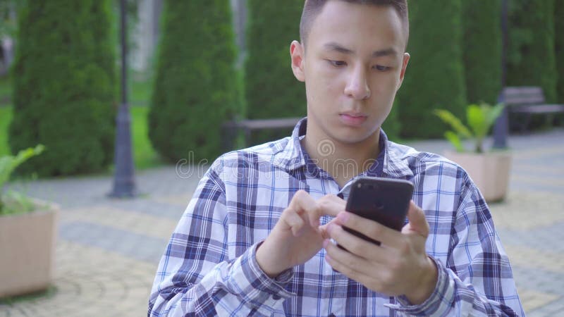 Un jeune homme asiatique handicapé dans un fauteuil roulant dans le parc et utilise un smartphone