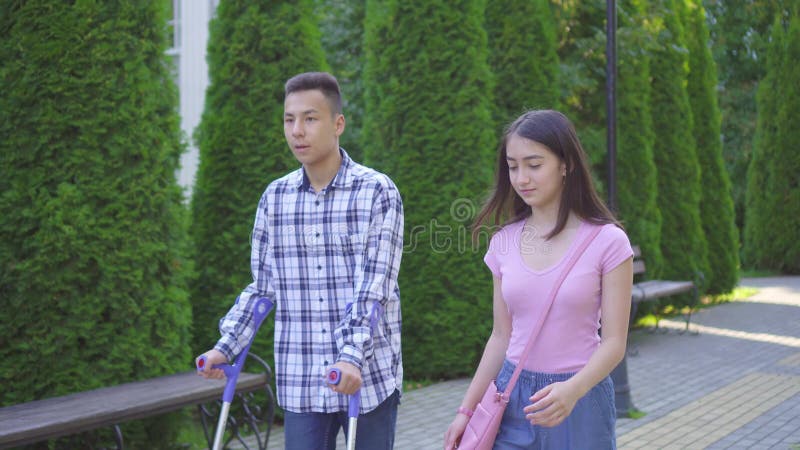 Un jeune homme asiatique qui a une jambe cassée sur des béquilles communique avec une jeune femme asiatique dans le parc