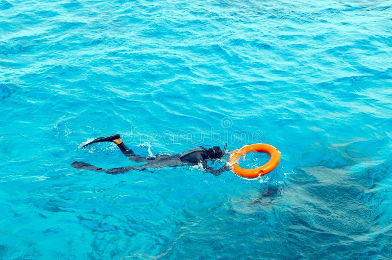 Un jeune homme dans un costume de plongée et bains de nageoires en mer tenant la bouée de sauvetage photographie stock Un jeune homme dans un costume de plongée et bains de nageoires en mer tenant la bouée de sauvetage photographie stock
