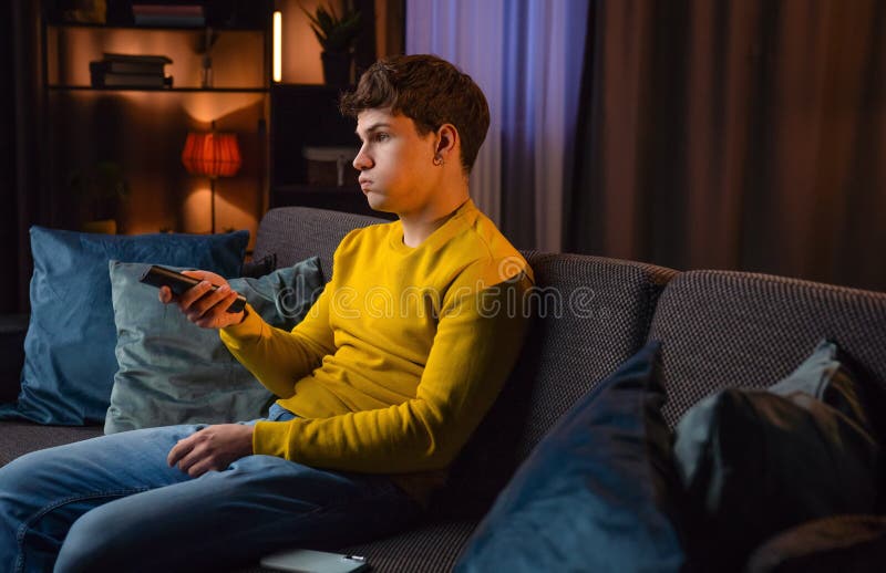 Un jeune homme dans la soirée après le travail se détendre à la maison assis sur le canapé dans le salon regarder programme à la t photo stock