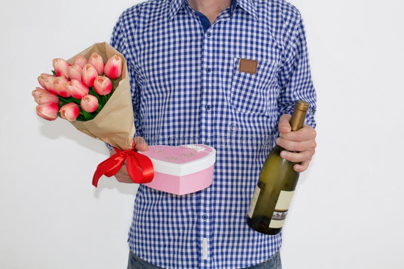 Un jeune homme dans une chemise et des jeans de plaid bleue, tenant un bouquet des tulipes, un boîte-cadeau en forme de coeur et photo stock Un jeune homme dans une chemise et des jeans de plaid bleue, tenant un bouquet des tulipes, un boîte-cadeau en forme de coeur et photo stock