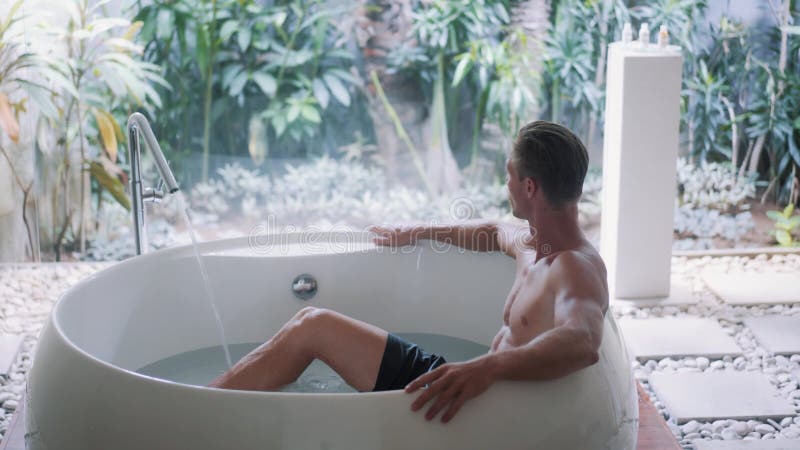 Un jeune sportif au corps musclé se repose dans une grande baignoire à la maison