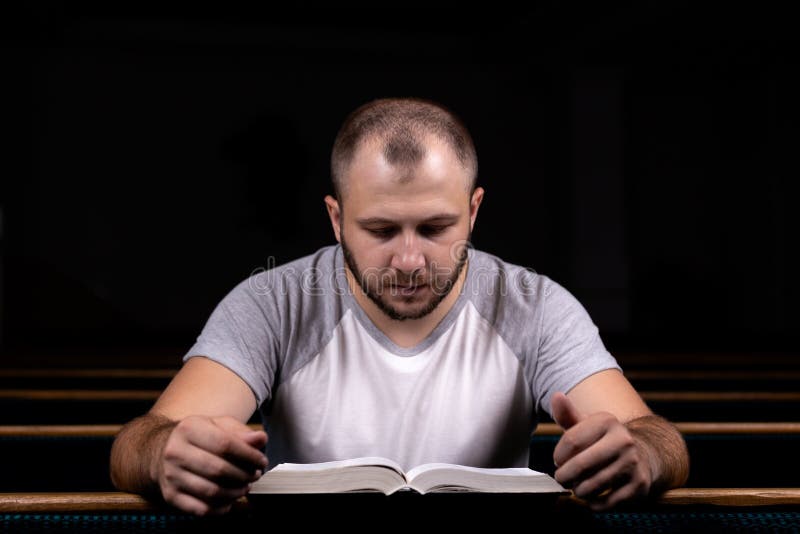Un jeune type s'assied sur un banc d'église, lit la bible et prie Le concept de la religion, prière, foi images libres de droits Un jeune type s'assied sur un banc d'église, lit la bible et prie Le concept de la religion, prière, foi images libres de droits