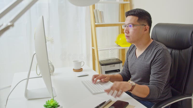 Un joven asiático adulto trabaja en casa o en una oficina moderna, usando computadoras de escritorio y smartphones Concepto de tr