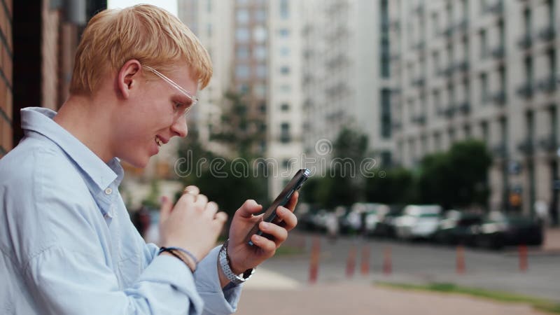 Un joven caucásico con ropa casual y gafas parado mirando el smartphone se sorprende metrajes