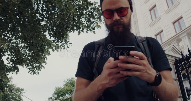 Un joven con barba está usando su smartphone al aire libre mientras disfruta de la luz del día metrajes