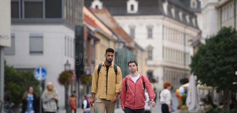 Un joven con síndrome de Down y su amigo mentor caminando por la ciudad hablando. fotografía de archivo libre de regalías