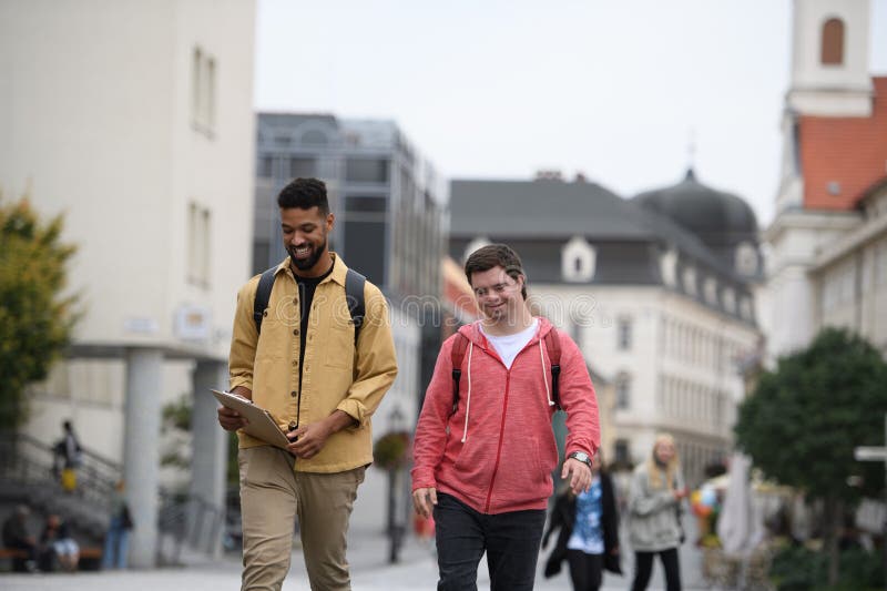 Un joven con síndrome de Down y su amigo mentor caminando por la ciudad hablando. fotografía de archivo