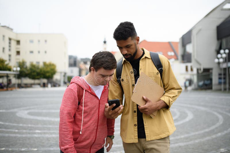 Un joven con síndrome de Down y su amigo mentor mirando algo en el smartphone. imagen de archivo libre de regalías