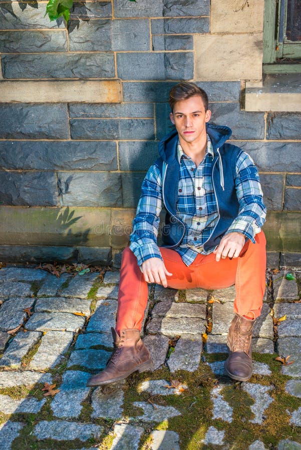 Un joven está sentado en el suelo contra la pared relajándose foto de archivo