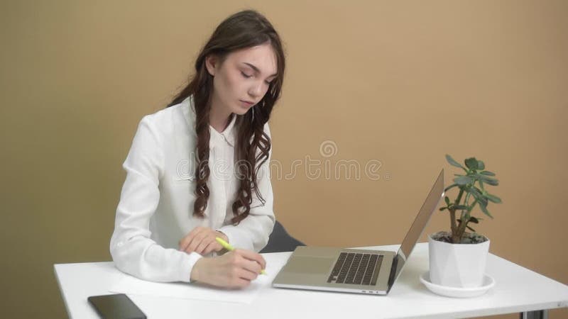 Un joven profesional toma notas desde un portátil en un espacio de trabajo minimalista con una planta almacen de metraje de vídeo